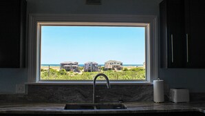 A kitchen with a large window overlooking a beach with houses. - 4X4 beach. Private Pool opens in May (Corolla)