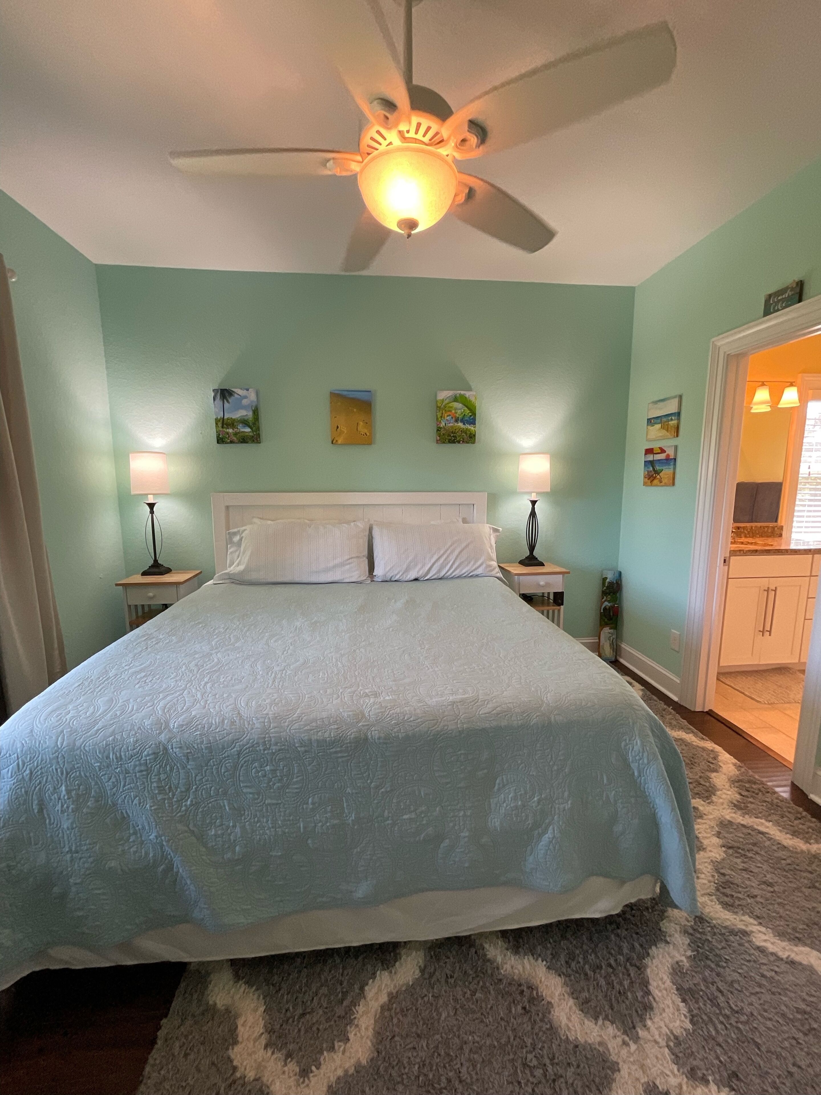 Quarto com cama, ventoinha no teto e obras de arte nas paredes.