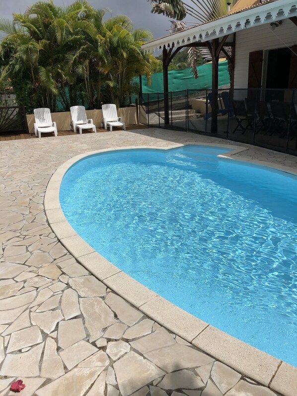 Una piscina con baldosas de piedra, sillas de descanso blancas y palmeras.