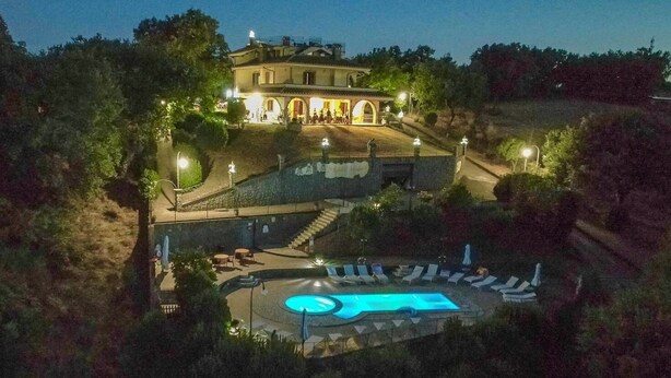 Ein großes Gebäude mit Schwimmbad, umgeben von Bäumen und einer gut beleuchteten Terrasse.