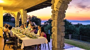 Ein langer Esstisch, gedeckt für eine Mahlzeit, mit Blick auf den Sonnenuntergang und die Landschaft.