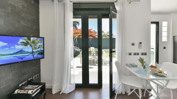 Een moderne woonkamer met een flatscreen televisie, een zwarte mediakast en een eethoek met witte stoelen en een tafel.