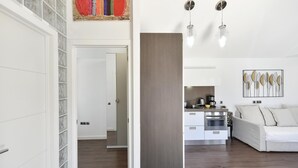 Een moderne woonkamer met een witte bank, een keuken met een koffiezetapparaat en een eettafel.
