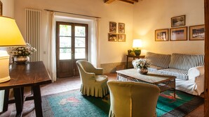 Uma sala de estar acolhedora com teto de madeira, um sofá, uma poltrona, uma mesa com abajur e uma janela com cortinas.