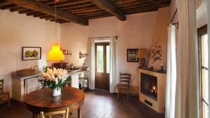 Uma área de jantar acolhedora com mesa de madeira, cadeiras, um vaso de flores e um candeeiro pendente.