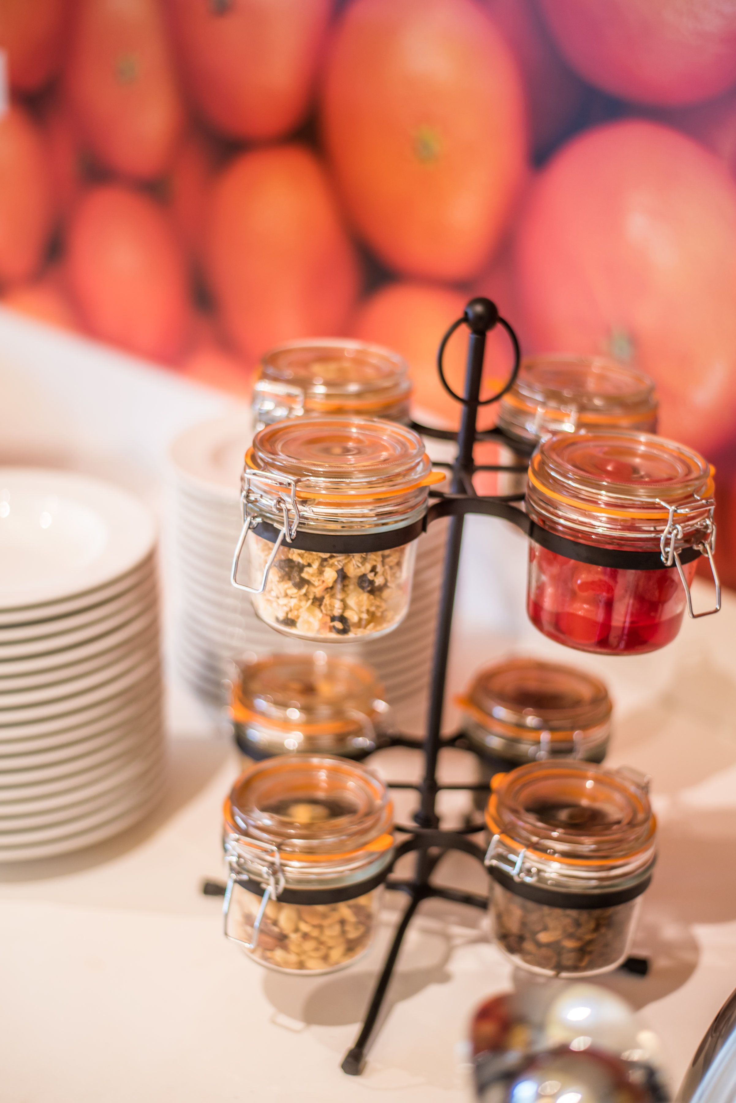Esposizione di cibi con barattoli contenenti vari snack e frutta, disposti su un espositore con piatti sottostanti.