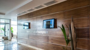 A reception area with a wooden panel wall, a digital display, and a potted plant. - Hampton by Hilton Santo Domingo Airport (Boca Chica)