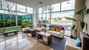 A spacious lobby with large windows, a seating area with sofas and coffee tables, and a small cart. - Hampton by Hilton Santo Domingo Airport (Boca Chica)