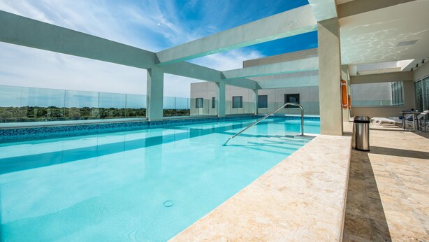 A modern indoor pool with clear blue water, a metal ladder, and a view of the sky and distant landscape. - Hampton by Hilton Santo Domingo Airport (Boca Chica)