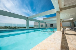 Une piscine intérieure moderne, avec une eau d’un bleu limpide, un escalier en métal et une vue sur le ciel et le paysage lointain.