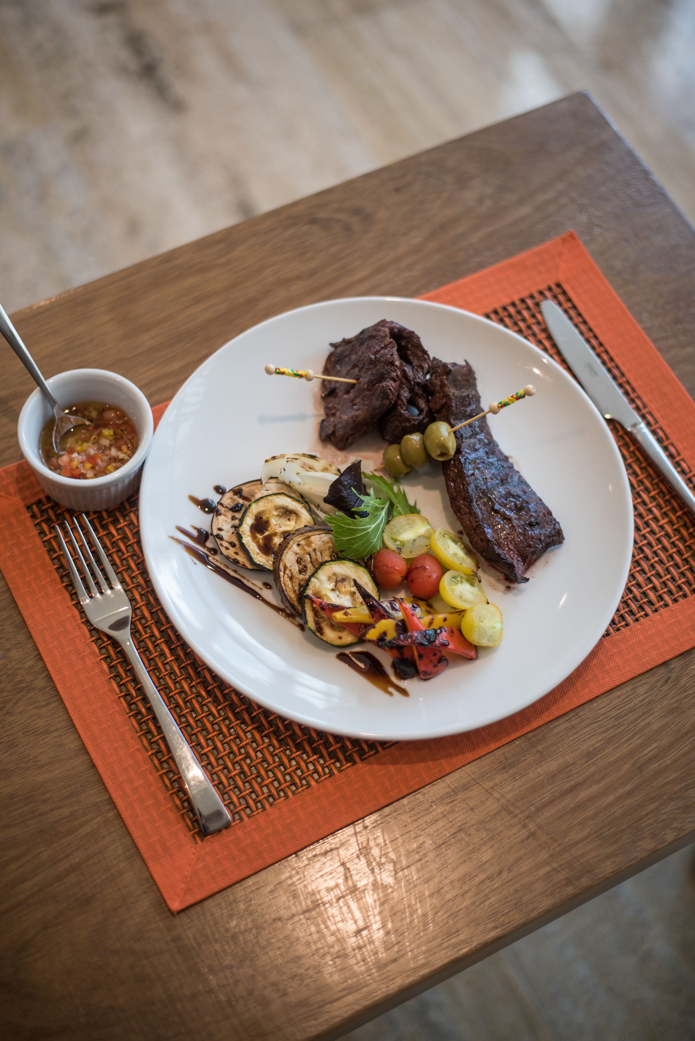 Une assiette de nourriture comprenant des légumes grillés et un steak, accompagnée d’un petit bol de sauce.