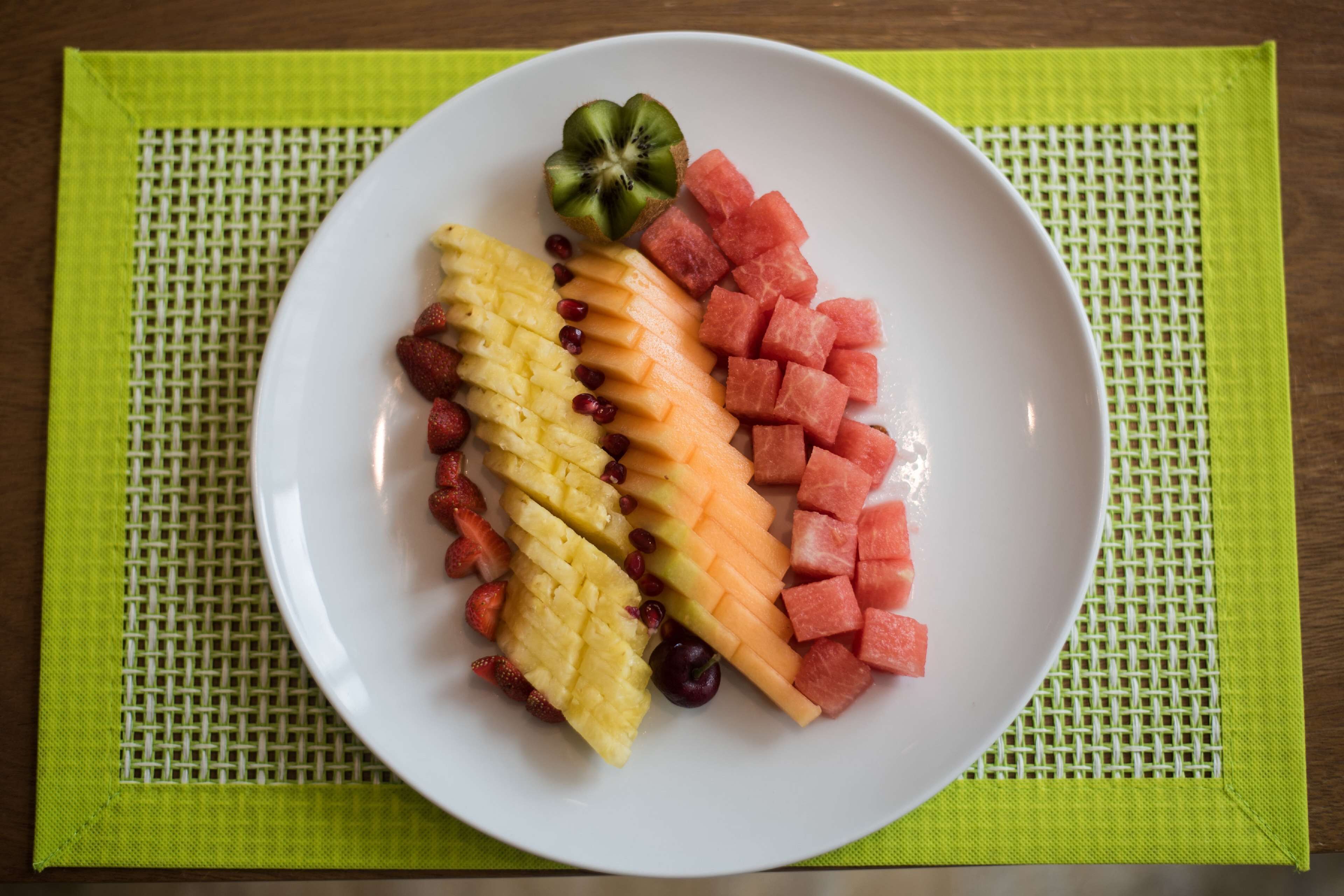 Un piatto bianco con frutta a fette e un kiwi su un sottopiattino verde.
