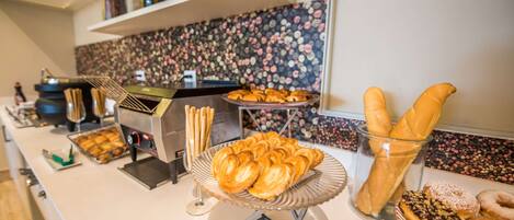 Un bufé con diversas pastas y pan, una máquina de café y una pared decorativa.