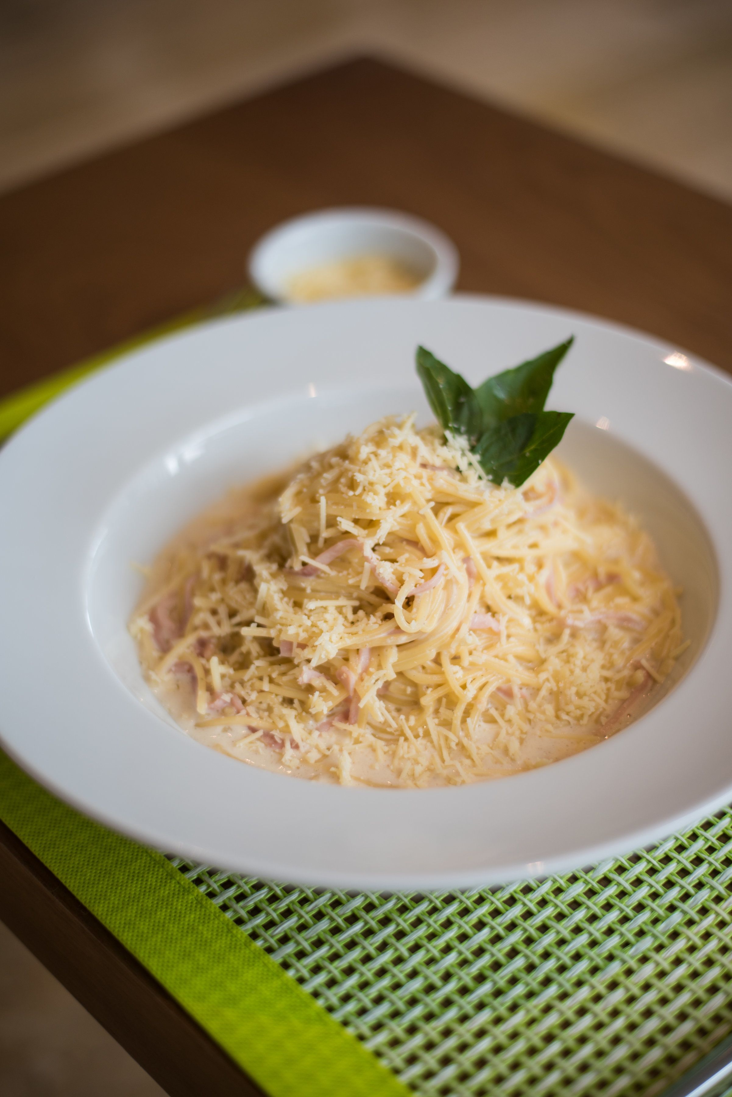 A white bowl of pasta with cheese and basil on a green placemat.