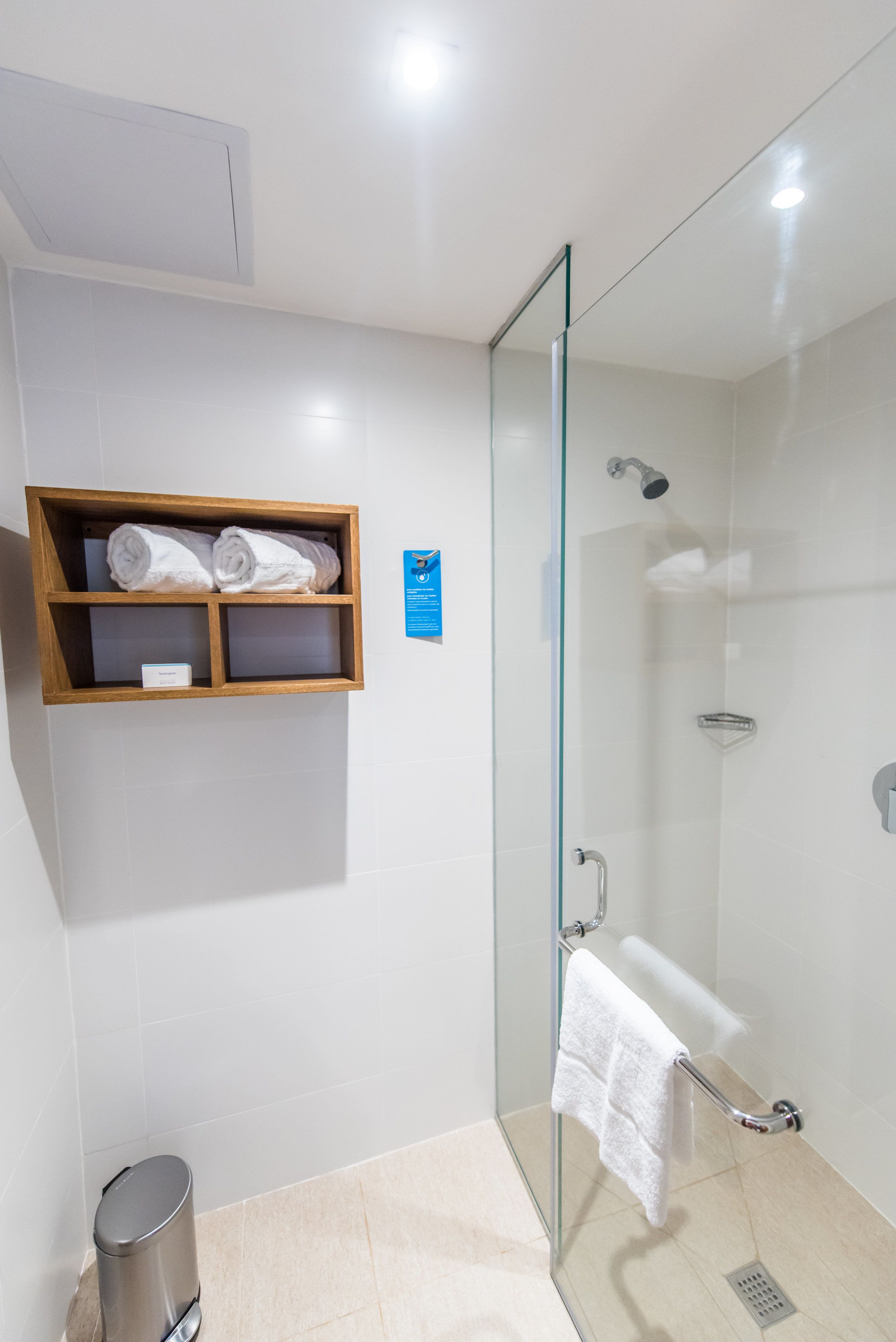 Ein modernes Badezimmer mit Duschkabine aus Glas, einem hölzernen Ablagebrett mit Handtüchern und einem Mülleimer.