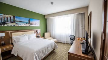 Habitación de hotel con una cama grande, un escritorio con computadora, una silla y un cuadro con una playa.
