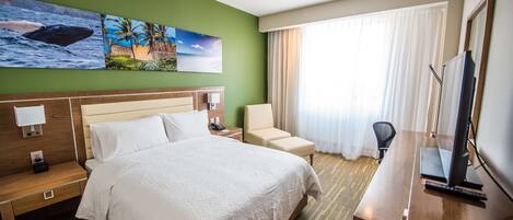 Una habitación de hotel con cama, escritorio, computadora, silla y televisión.
