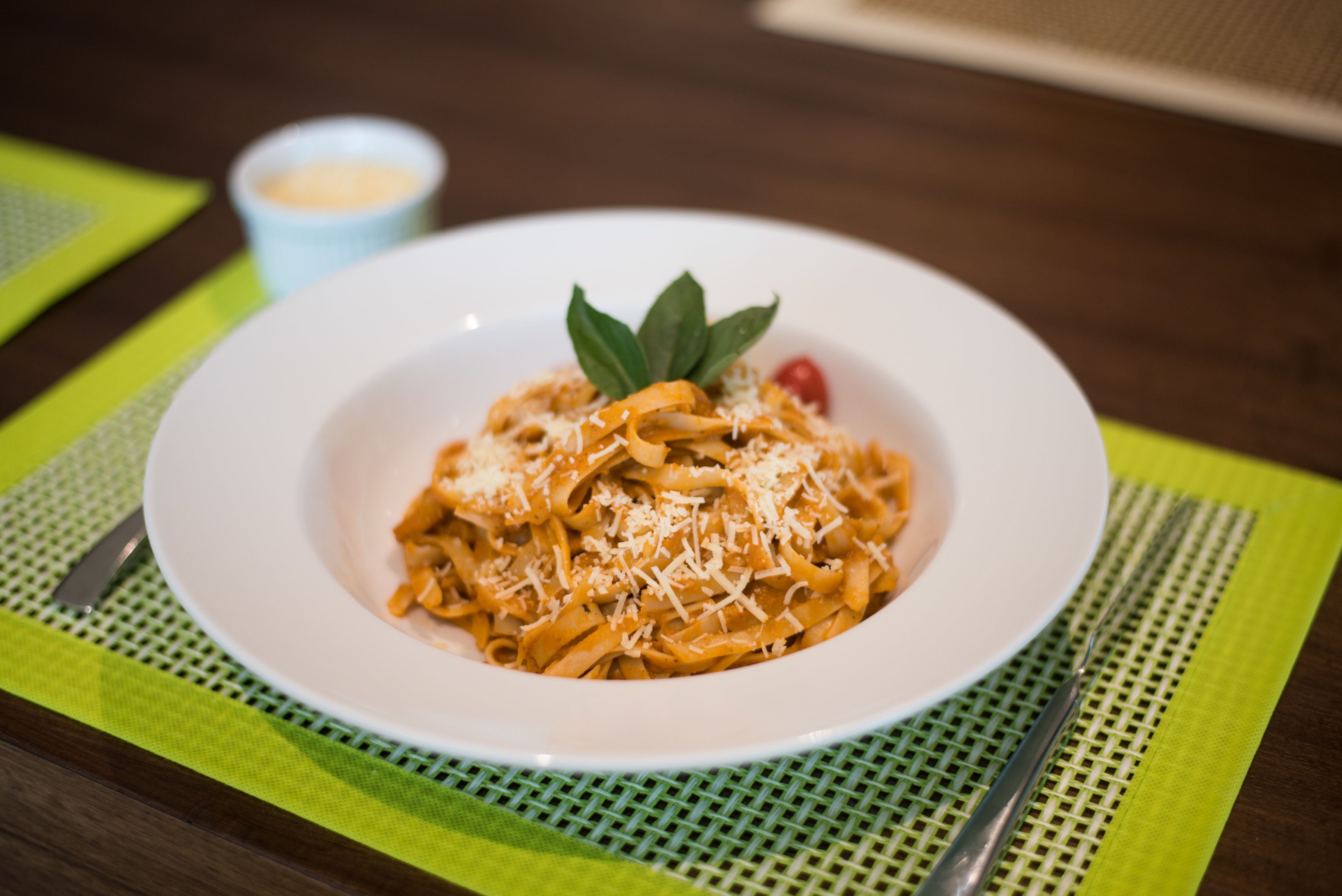 A white plate of pasta with grated cheese and a garnish on a green placemat.