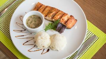 A plate with grilled salmon, a small bowl of sauce, and two scoops of ice cream on a white plate, placed on a green placemat.