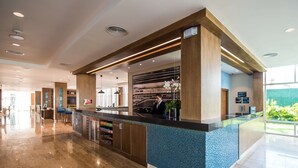 A modern reception area with a wooden reception desk, a blue-tiled counter, and a large window offering a view of the outdoors. - Hampton by Hilton Santo Domingo Airport (Boca Chica)