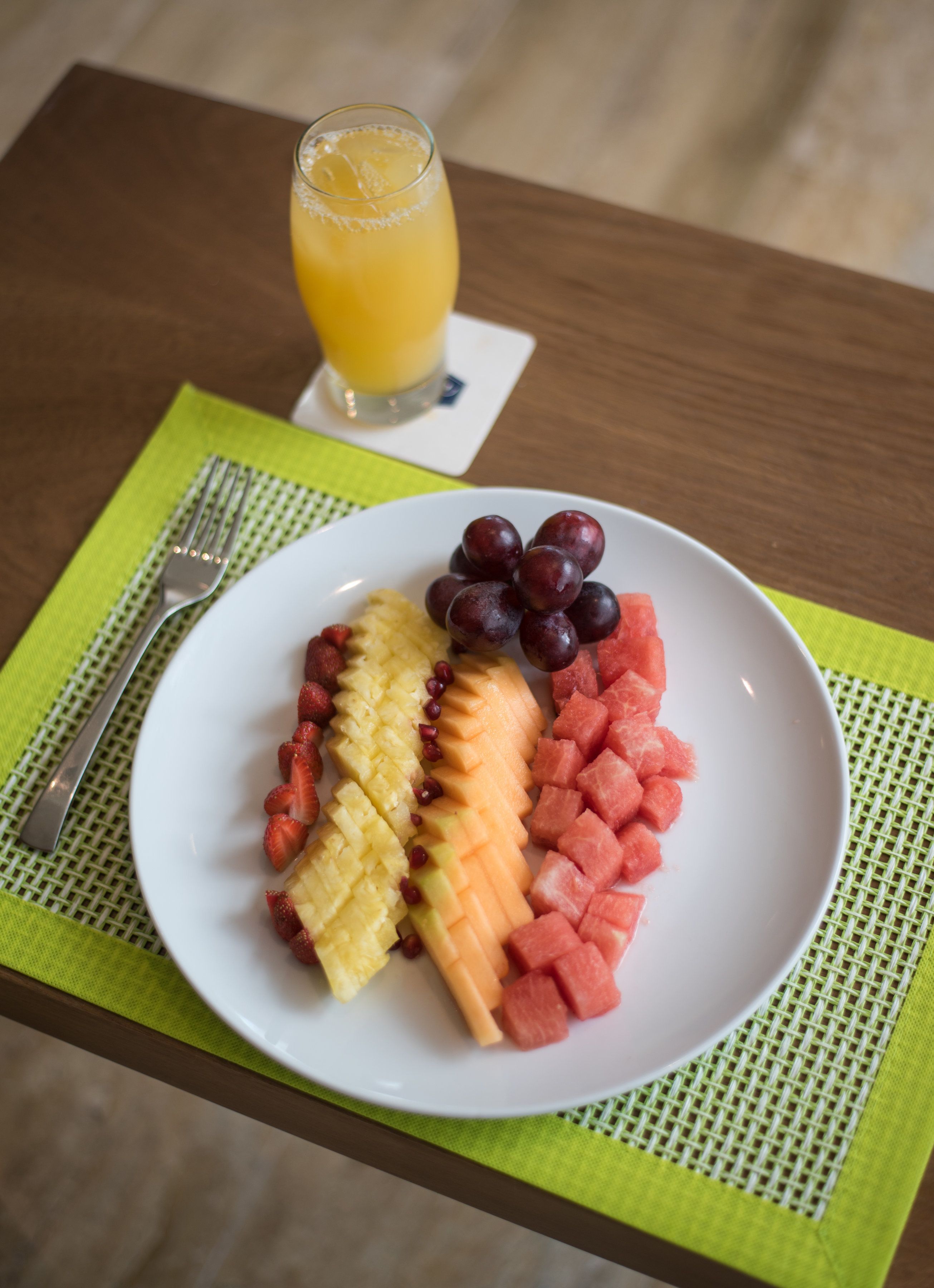A plate of sliced fruits and a glass of orange juice on a table.