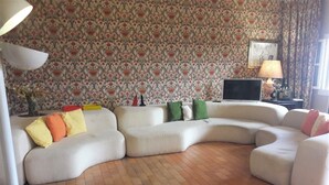 Un salon avec un canapé d’angle, un téléviseur à écran plat et un papier peint à motifs.