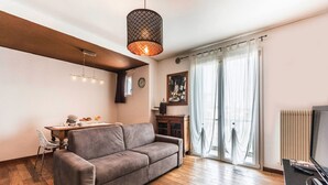 A modern living room with a grey sofa, wooden flooring, a hanging light fixture, and a large window with sheer curtains. - Novalesi Apartment (20 minutes from Venice) (Noale)