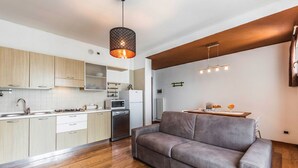 A modern kitchen with wooden cabinets, a built-in microwave, and a dining area with a grey sofa and a small table. - Novalesi Apartment (20 minutes from Venice) (Noale)