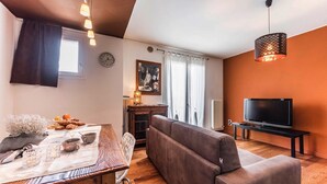 A cozy living room with a sofa, a dining table with a vase and snacks, a TV on a stand, and a clock on the wall. - Novalesi Apartment (20 minutes from Venice) (Noale)