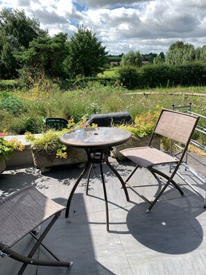 An outdoor patio with a round table and two chairs, surrounded by lush greenery and flowers. - Peaceful Pigsty – Countryside Retreat near the Cotswolds & Cheltenham / Sleeps 6 (Pershore)