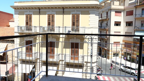 A multi-story building with balconies, a street view, and a clear sky.
