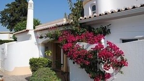 A white building with a small tower, a covered entrance, and pink flowering plants. - Beautiful Residential Villa on An Exclusive Private Complex, pool, roof terrace (Carvoeiro)
