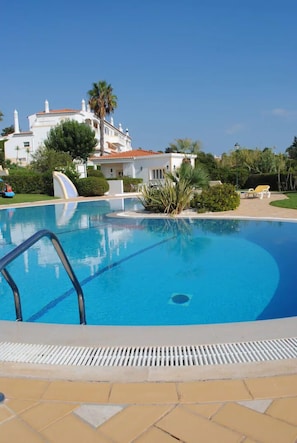 A swimming pool with a clear blue water, surrounded by a tiled deck and a white building with a red roof in the background. - Beautiful Residential Villa on An Exclusive Private Complex, pool, roof terrace (Carvoeiro)