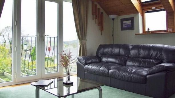A living room with a leather sofa, a glass coffee table, and a view through large windows.