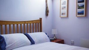 A bedroom with a wooden headboard, a bed with striped bedding, a bedside table with a lamp, and framed pictures on the wall.