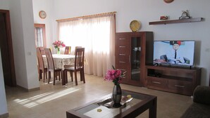 Una sala de estar con comedor, televisor y un florero con flores.