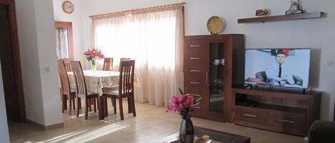 A living room with a dining area, a TV, and a vase with flowers.