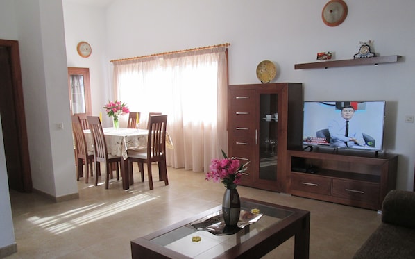 A living room with a dining area, a TV, and a vase with flowers.