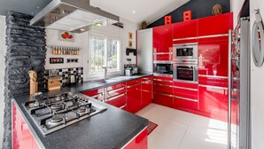 Een moderne keuken met rode kastjes, een gasfornuis en roestvrijstalen apparatuur.