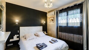 Een moderne slaapkamer met een groot bed, nachtlampjes, een kroonluchter en een raam met gordijnen.