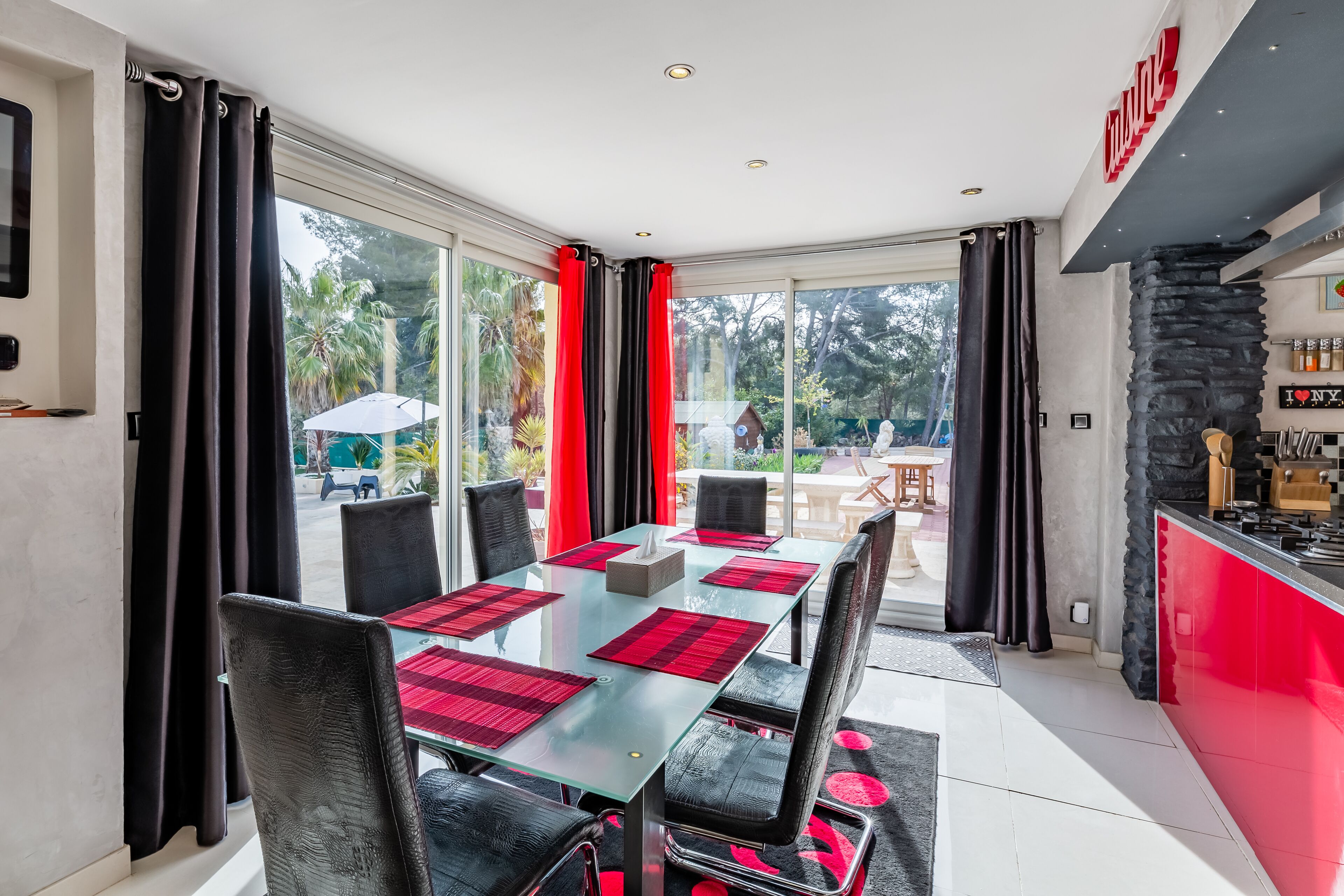 Un espace repas moderne avec une table en verre, des chaises noires et des sets de table rouges.
