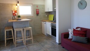 Una cucina compatta con lavastoviglie integrata, un divano rosso con cuscini decorati e una sveglia a parete.