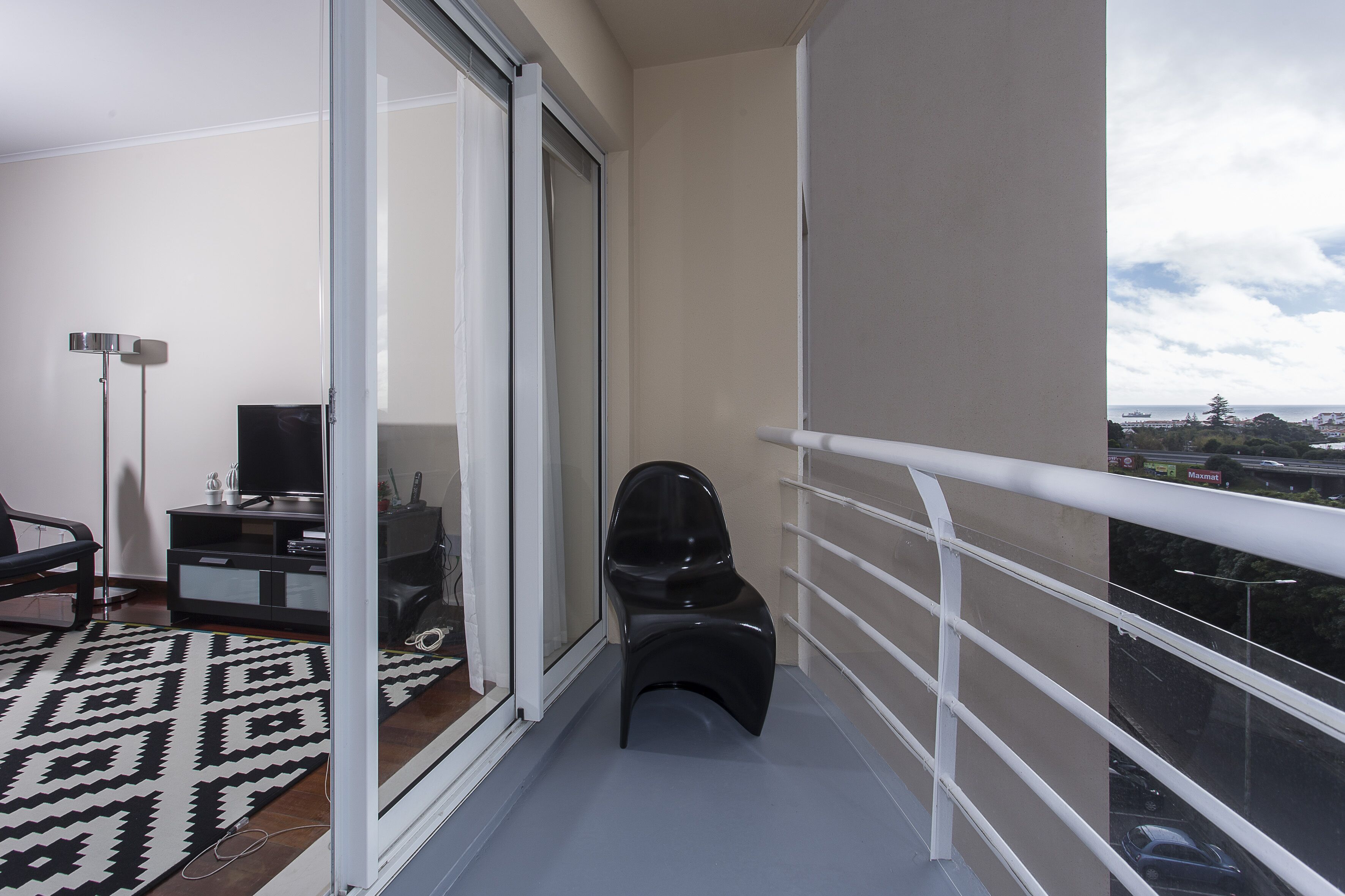A balcony with a black chair, a TV on a black stand, and a patterned rug.