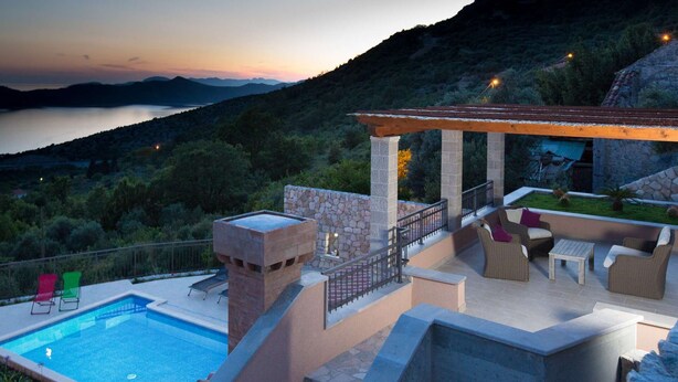 Zona de piscina con vistas a un lago y montañas al anochecer.