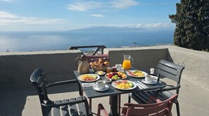 Ein Tisch mit Frühstücksleckereien wie Eiern, Speck und Obst, mit Blick auf eine schöne Landschaft.