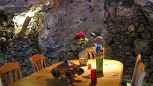 Ein rustikaler Esstisch vor einer Wand aus Stein, ein Holzstuhl, eine Vase mit roten Blumen und eine kleine Figur.