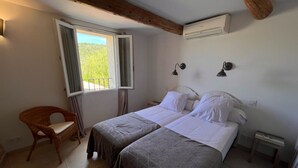 A bedroom with two beds, a chair, a window, and a wall-mounted air conditioner.