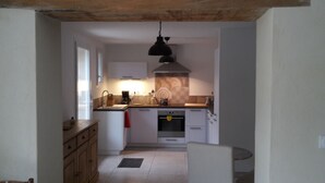 A compact kitchen with white cabinets, a wooden countertop, a built-in oven, and a hanging pendant light.