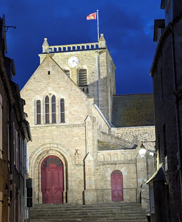 A historic stone building with a clock tower, arched windows, and a flag.
