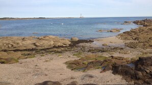 Una costa rocosa con aguas tranquilas y un faro distante.